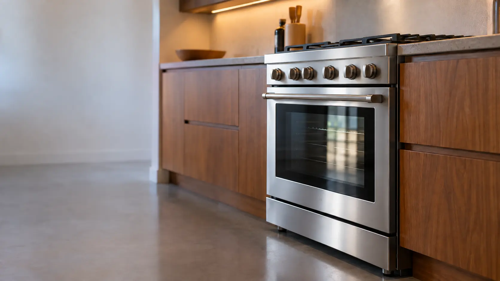 A kitchen with the range in a mid-century house kitchen with a range in teak cabinets, seen from a low angle, the oven door glass catching the light.