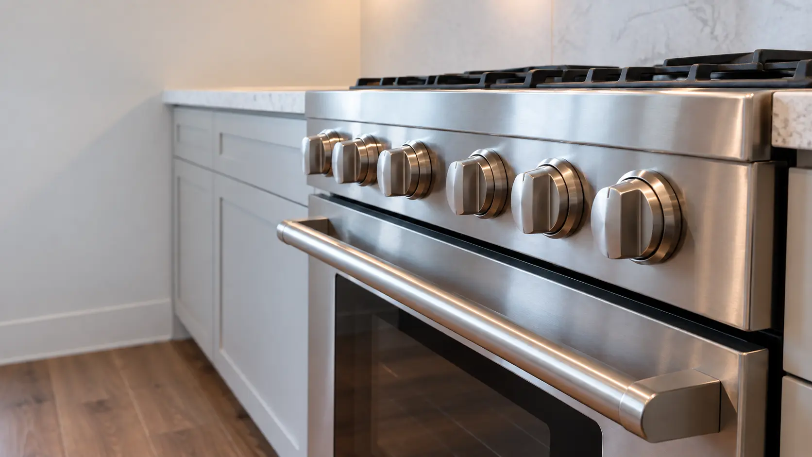 The control knobs and oven door handle of a stainless range filling the frame, soft light.