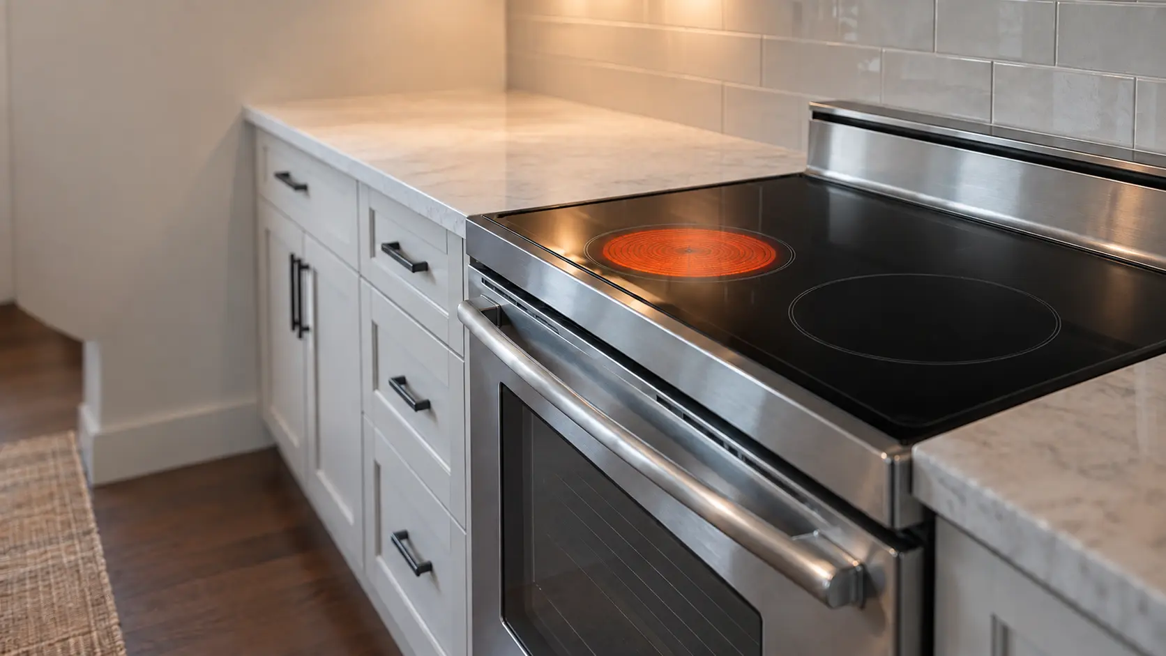 The smooth black glass top of an electric range with one round zone glowing a dull orange and the zone beside it cold and dark.
